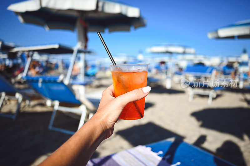 女人手里拿着橙汁鸡尾酒。夏日饮料和海滩景观。