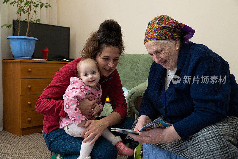 带着孩子的女人拜访了年长的女人。他们正在一起读一本儿童读物。