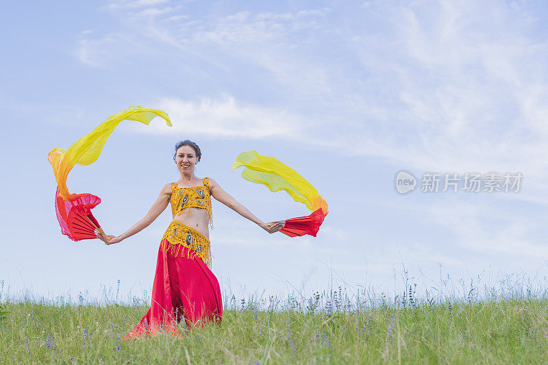 身着红色民族服饰的美女，在蓝天下的绿色田野上跳着东方舞蹈