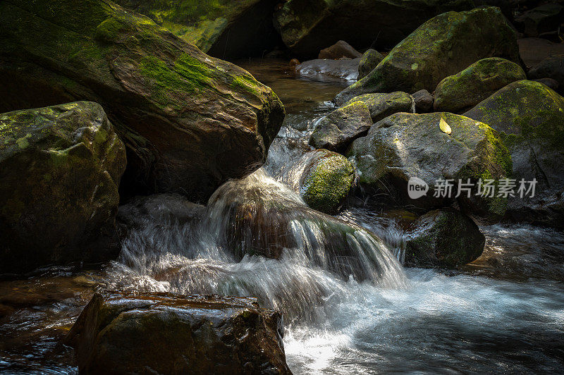 台湾基隆暖东谷，美丽的阳光照在长满青苔的岩石上，水像瀑布一样从河顶流下。