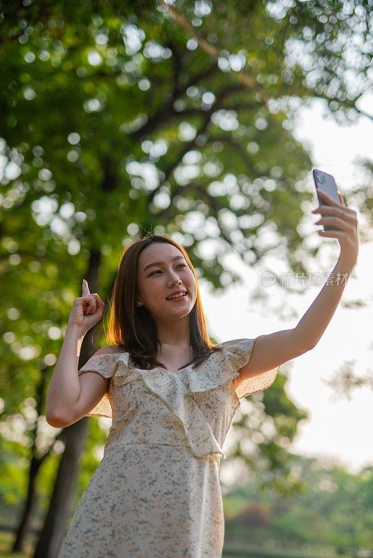 年轻的亚洲女子在公园用手机自拍。在郁郁葱葱的绿色森林里，美女视频通话