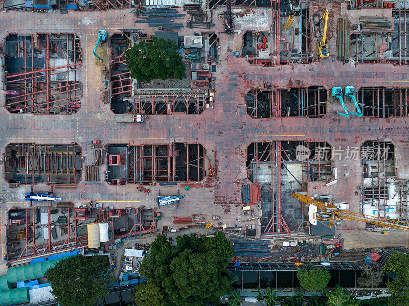 大型建筑施工现场的高角度空中俯视无人机视角，现场有许多大型起重机和机械车辆在白天工作。工业商业或土木工程技术概念。