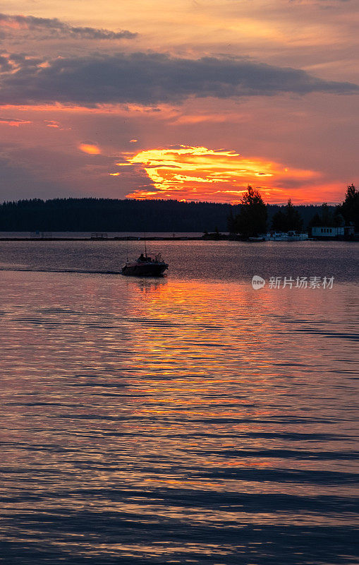 芬兰塞马湖上明亮的夕阳和一艘在夕阳下的机动渔船。夏天的风景