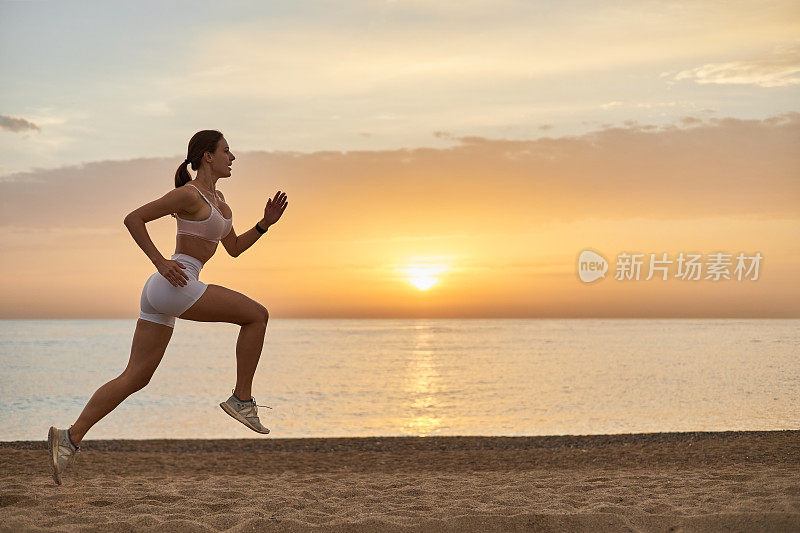 一个健康的女人在海边迎着明亮的日出慢跑