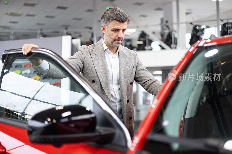 一名男子站在一辆红色轿车旁，向顾客推销新车