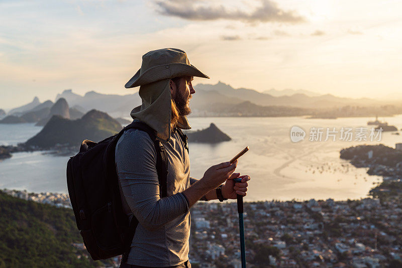 徒步旅行后，一名男子在山顶上使用智能手机