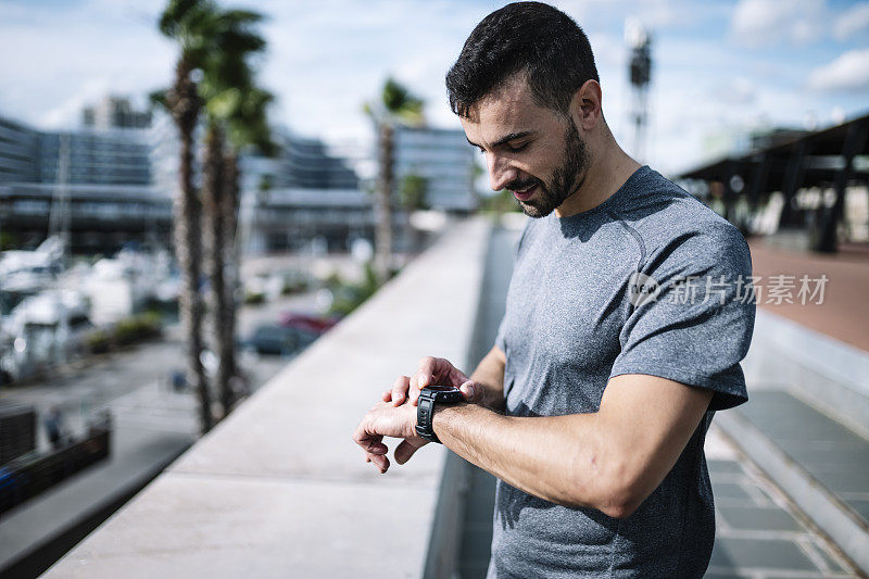 在外面运动时看起来很有活力的人。健身男在做完有氧运动后看他的智能手表查看跑步时间。