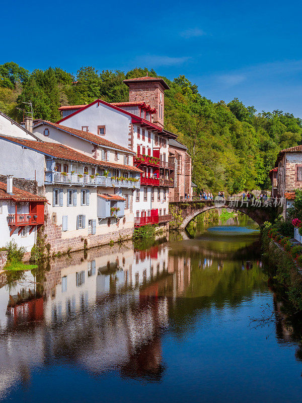 法国白色小镇的垂直景观，红色的阳台和鲜花被一条宁静的河流穿过。Saint-Jean-Pied-de-Port、法国
