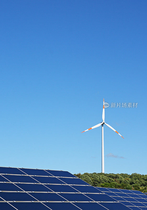 在晴朗的蓝天下，太阳能电池板后面的风力涡轮机