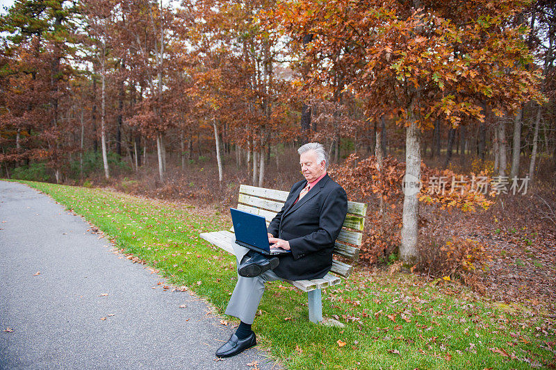 一个老人坐在公园的长椅上，拿着笔记本电脑