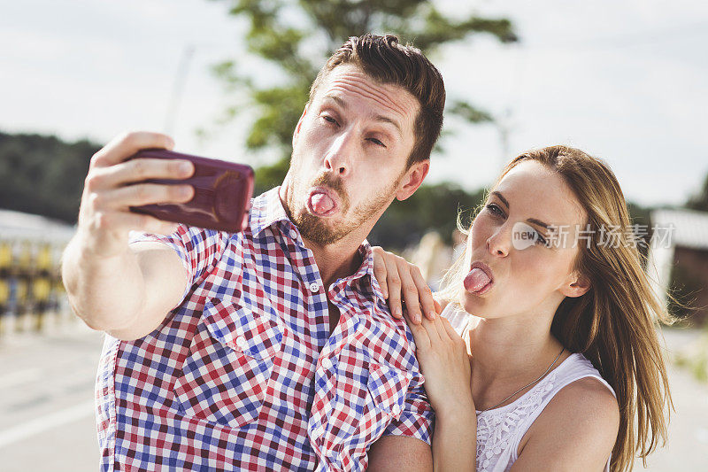 一对情侣拿着智能手机自拍，还伸出舌头