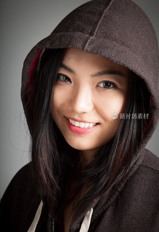 迷人的亚洲女孩穿着连帽衫在灰色的背景