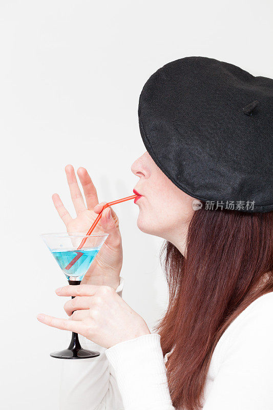 戴贝雷帽的女孩用吸管喝着蓝色鸡尾酒杯