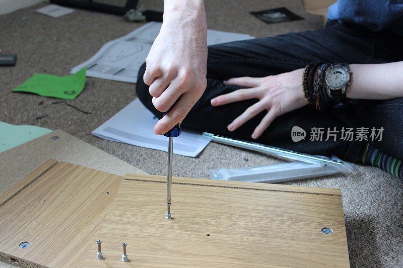 十几岁的男孩正在组装平装家具柜，用螺丝刀和螺丝自己动手