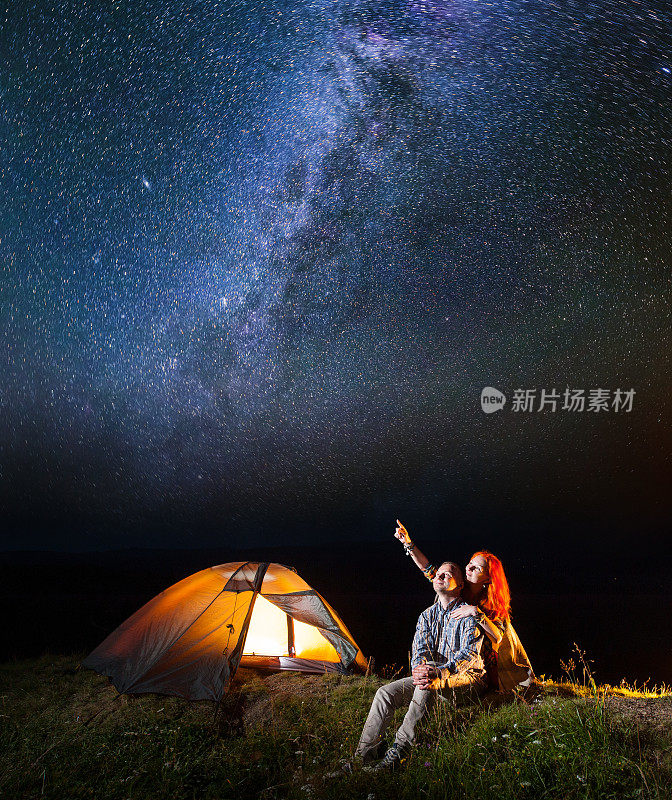一对游客夫妇，女孩和男孩看着夜空中闪耀的星空。两人坐在露营附近