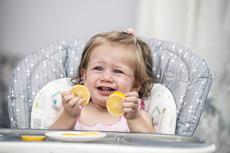 快乐的小女孩在高椅子上吃柠檬。