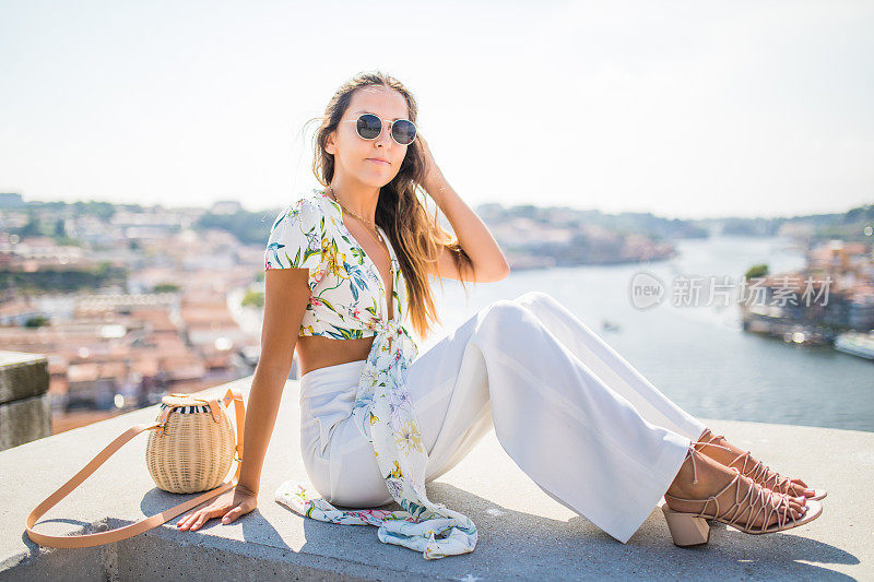 年轻漂亮的女人坐在观景台在杜罗河和多姆路易斯I桥在波尔图，葡萄牙。