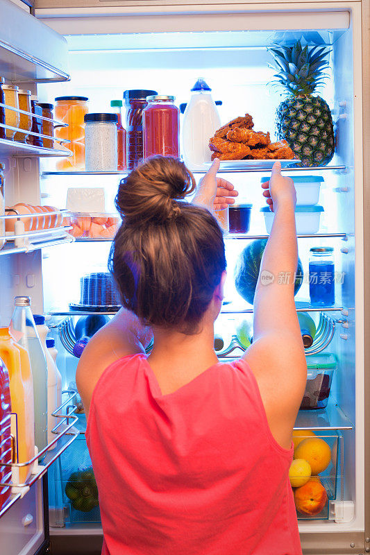 年轻女子在冰箱前决定吃不健康的食物