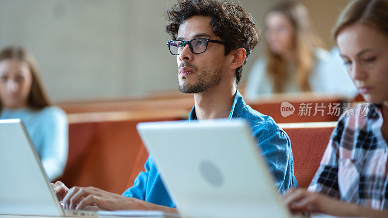 英俊的西班牙裔学生在大学听讲座时使用笔记本电脑。现代聪明学生的多民族群体。