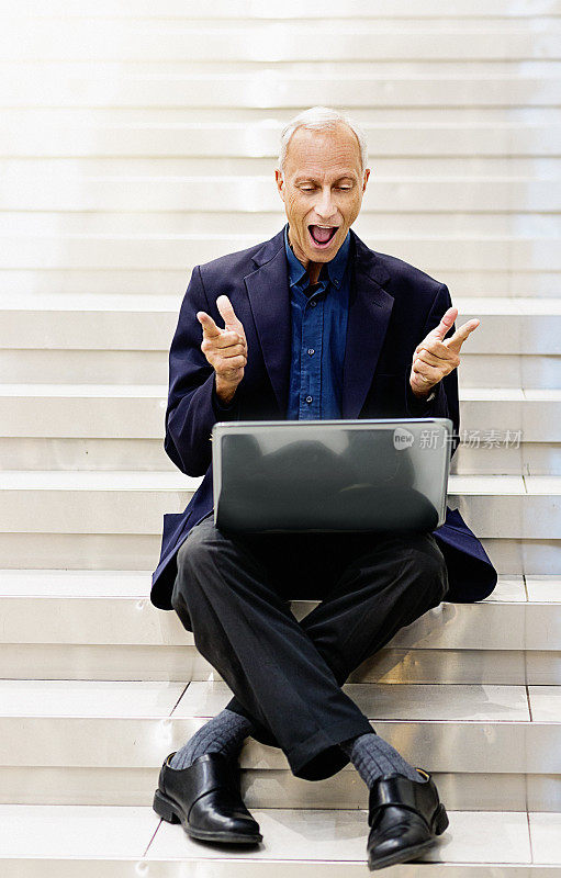兴高采烈的男人坐在大理石楼梯上，拿着笔记本电脑