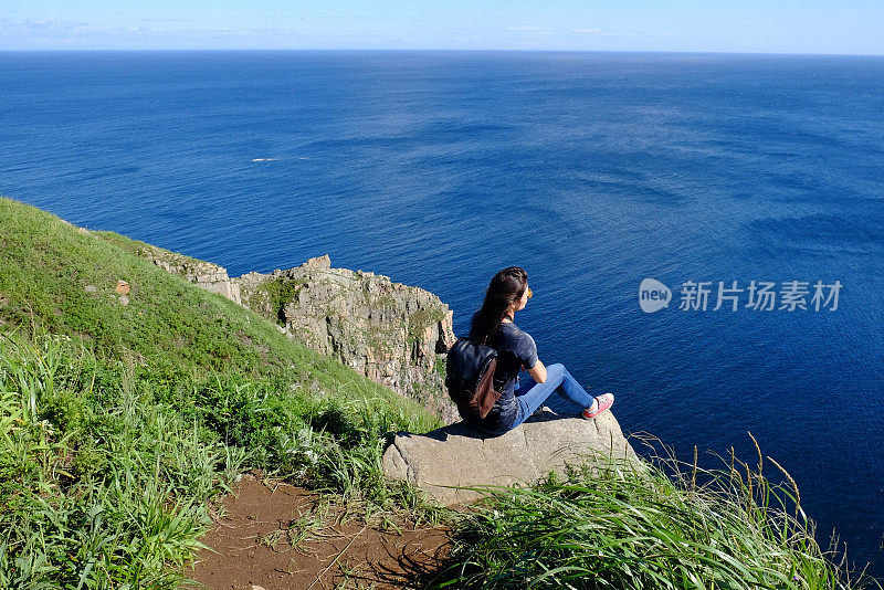 一个背着背包的女人坐在海边的岩石上。