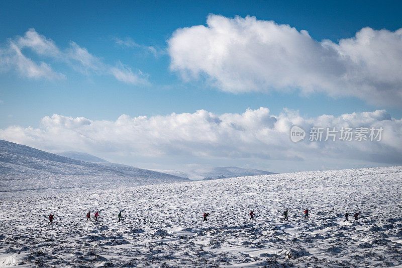 远处的一群人在冰雪覆盖的荒野中徒步旅行，远处的山脉和朦胧的阳光