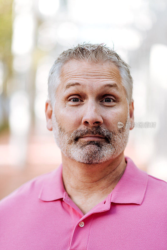 肖像成熟的白人男子灰色头发在粉红色polo衫与困惑的面部表情