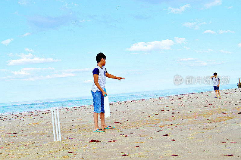 夏天的一天，两个孩子在海边的沙滩上打板球。
