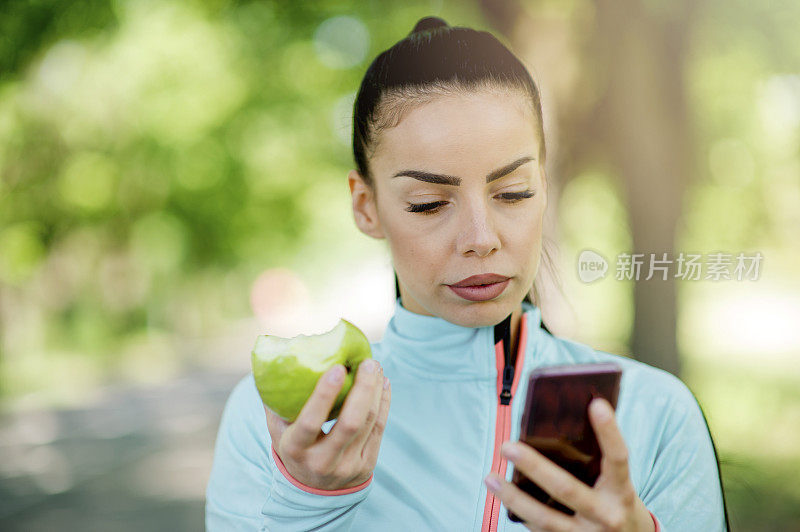 用智能手机吃苹果的女人的肖像