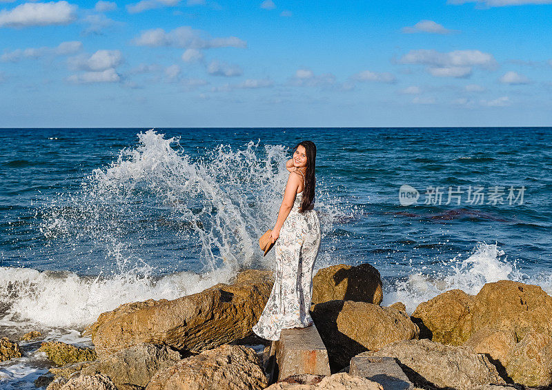 年轻漂亮的泰国裔柬埔寨裔美国妇女站在海边一块露出海面的岩石上