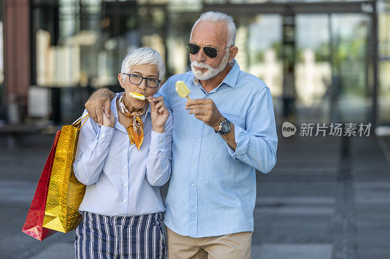 一对时尚的老夫妇在逛完购物中心后正在城市的街道上吃冰淇淋