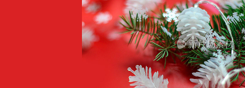由红色背景上的白色松果和圣诞树的树枝组成的圣诞花环。选择性聚焦，侧视图，拷贝空间。横幅