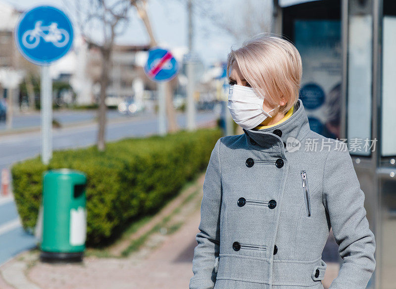 年轻妇女戴着口罩在街上等候