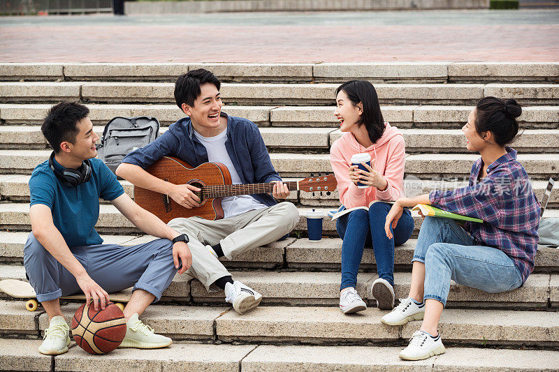 年轻的大学生坐在台阶上弹吉他唱歌