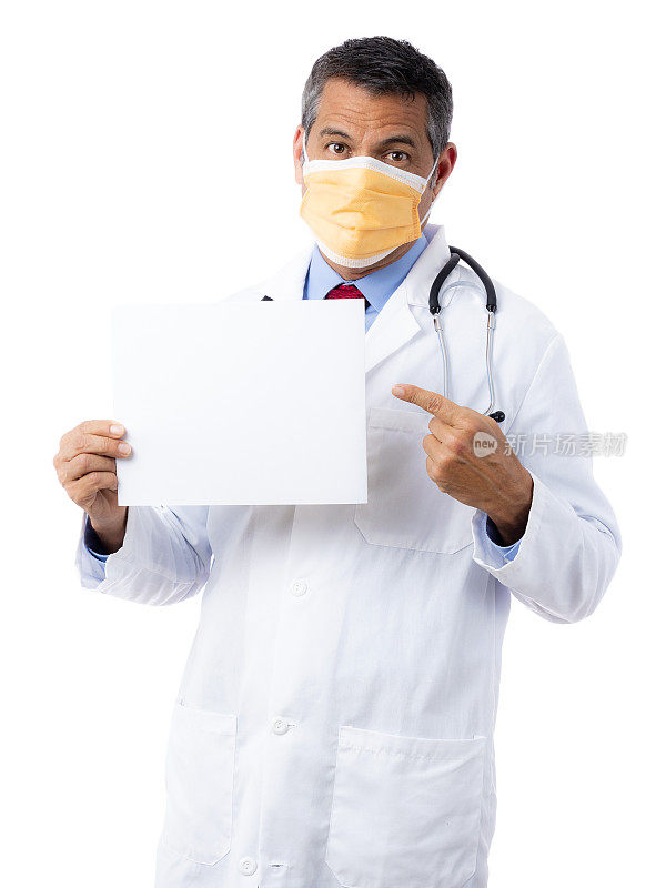 西班牙裔男医生穿着实验服，打着领带，戴着医用口罩，听诊器被隔离在白色背景上，手持白色指示牌并用左手指着它