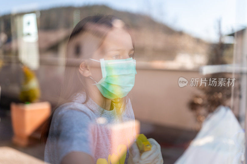 年轻的女孩戴着外科口罩和防护手套在家里擦窗户