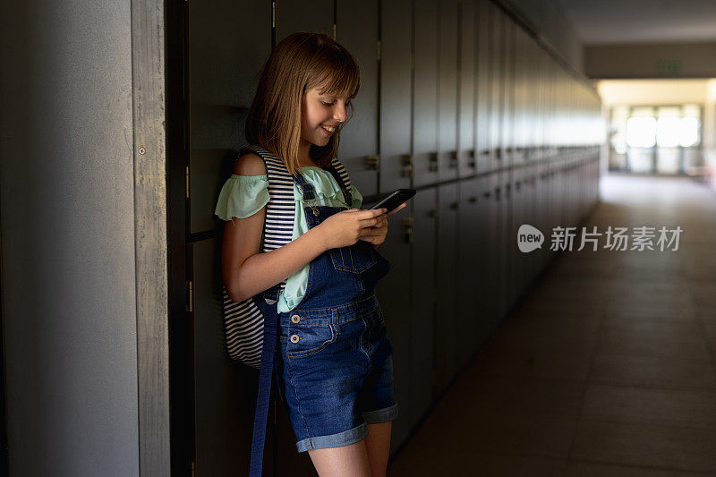 一名女生靠在走廊的储物柜上使用智能手机