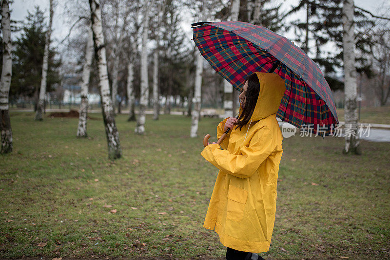 穿着黄色雨衣的年轻女子在公园里度过雨天