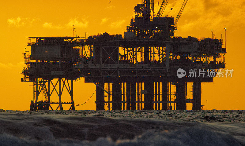 海浪与剪影的一个近海石油钻井平台在地平线上的距离日落