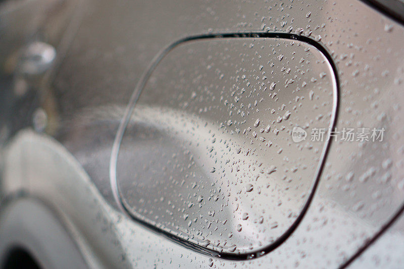 水滴从雨点滴在银色汽车的车身上，露珠盖在油箱的盖上，特写照片