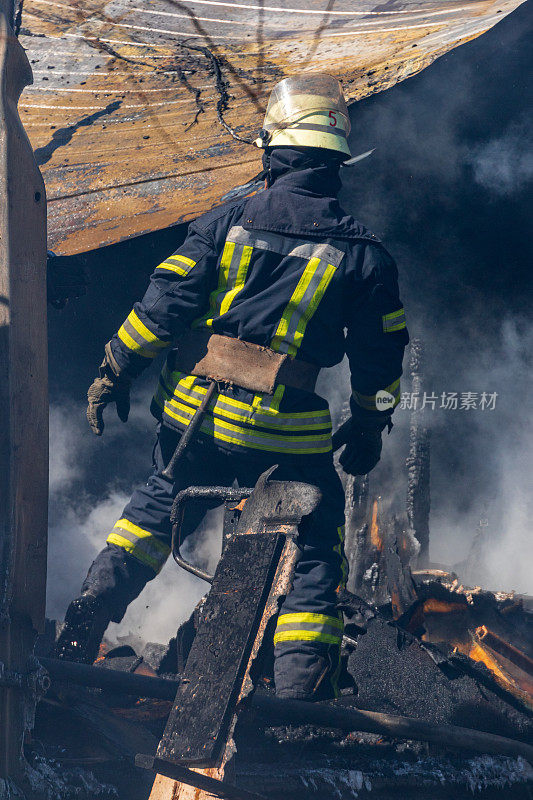 在一次消防行动中，一位强壮勇敢的消防员用水救出了一座正在燃烧的建筑物。穿着消防服的消防员。