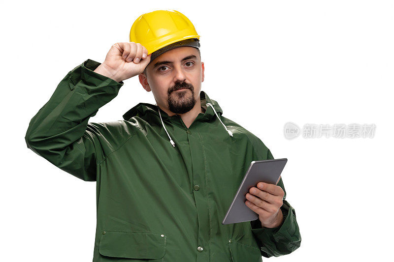 年轻工程师的肖像与绿色雨衣和安全帽看着相机和手持数字平板电脑