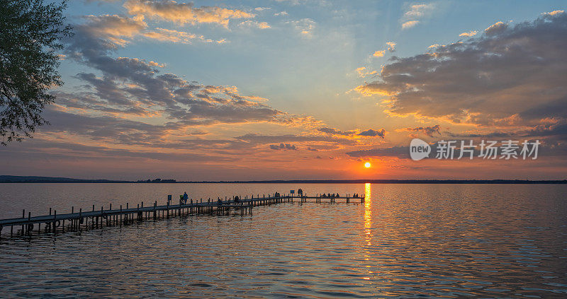 日落时，人们在湖边码头上的剪影与雄伟的云景