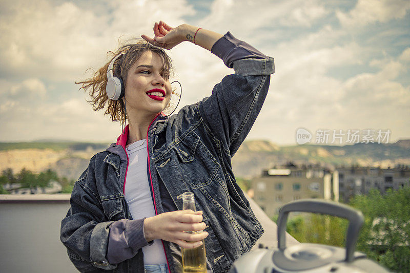 一个年轻的复古风格的女孩在楼顶听音乐-他在楼顶听音乐，享受自由，喝酒