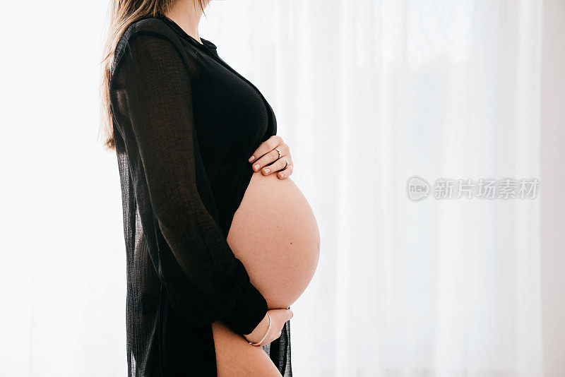 一名孕妇在白色背景下抚摸着自己的腹部