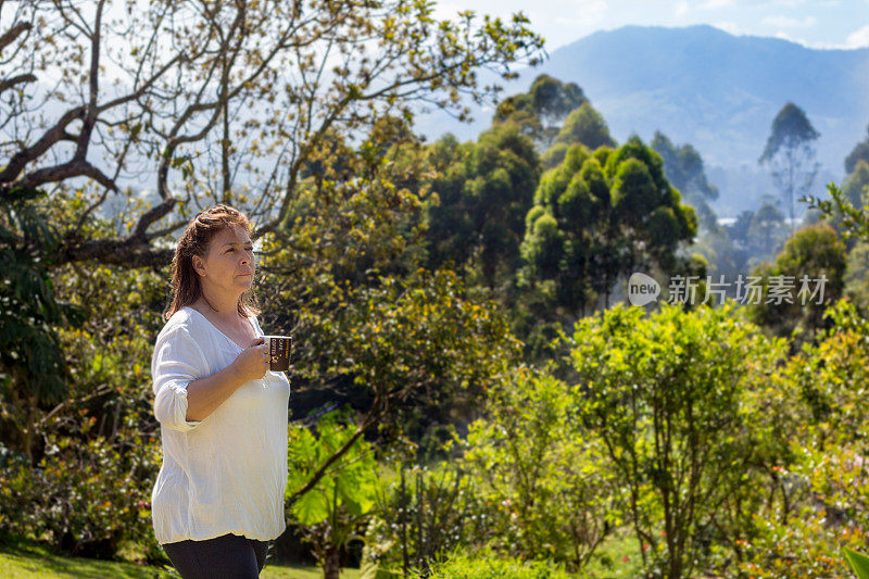 退休的成熟女人捧着一杯咖啡，望着蓝天