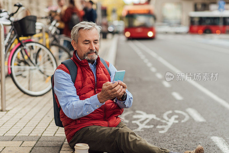 一名老年男子在街上用智能手机喝咖啡休息