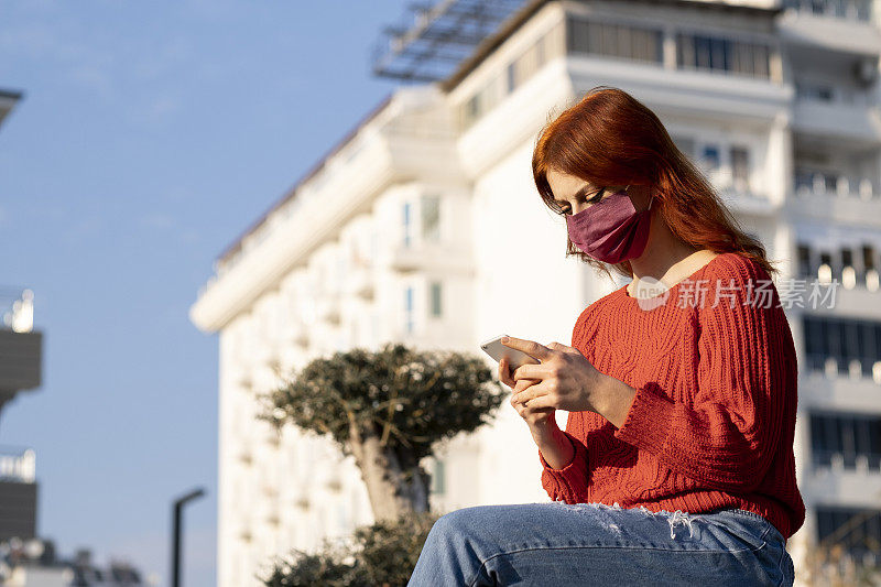 年轻女性戴着防护口罩在街上预防冠状病毒和防雾霾，使用智能手机的肖像