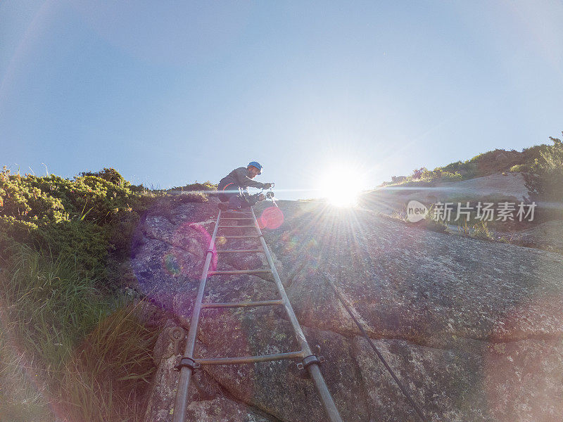 梯子上登山者的低角度视角，阳光