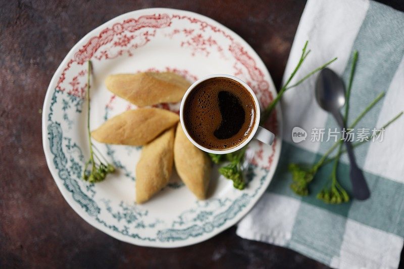 锈迹斑斑的背景上放着有花卉图案的陶瓷盘子，上面放着咸味饼干和一杯土耳其咖啡